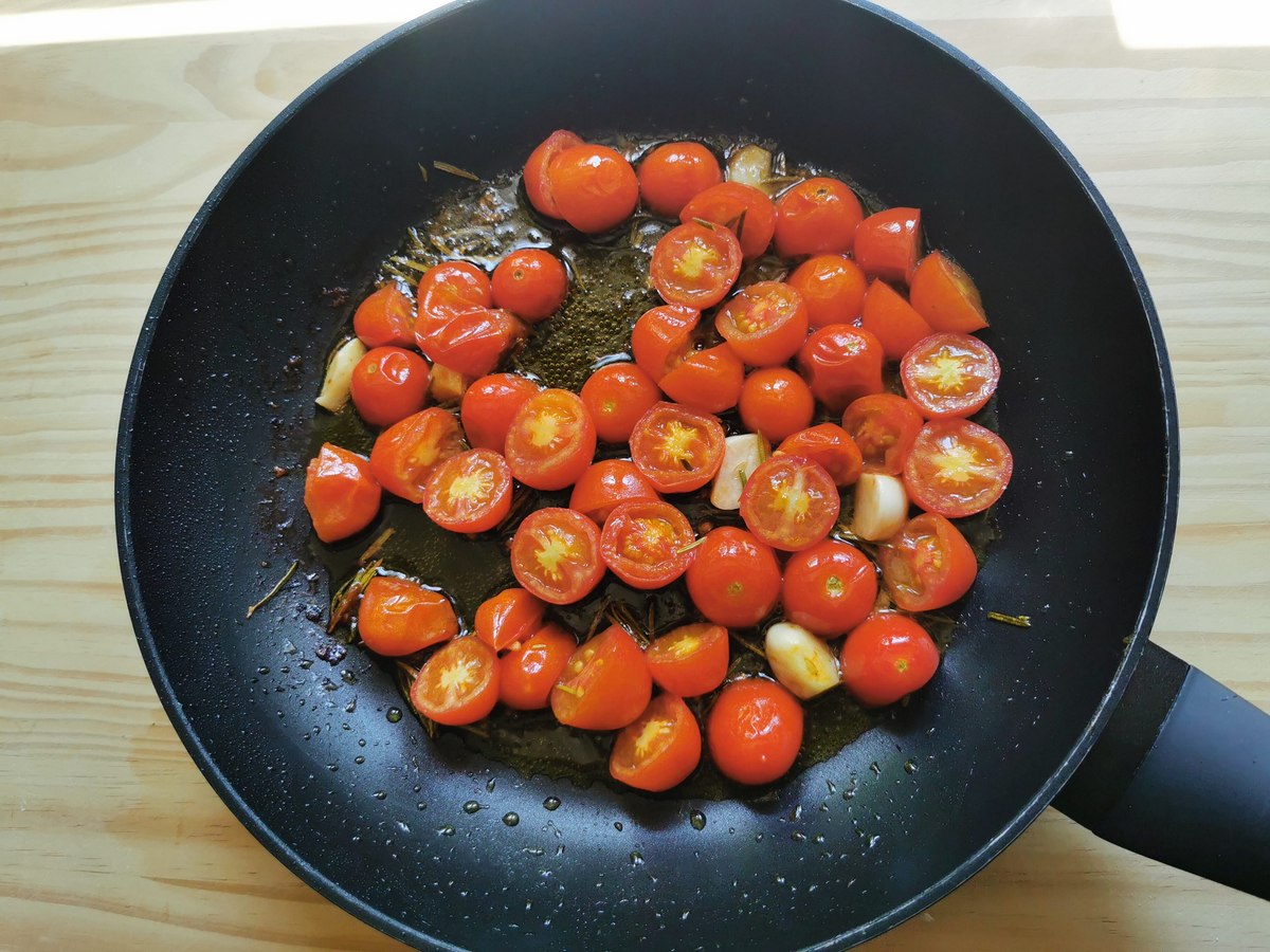 Halved tomatoes, garlic and rosemary cooking in skillet.