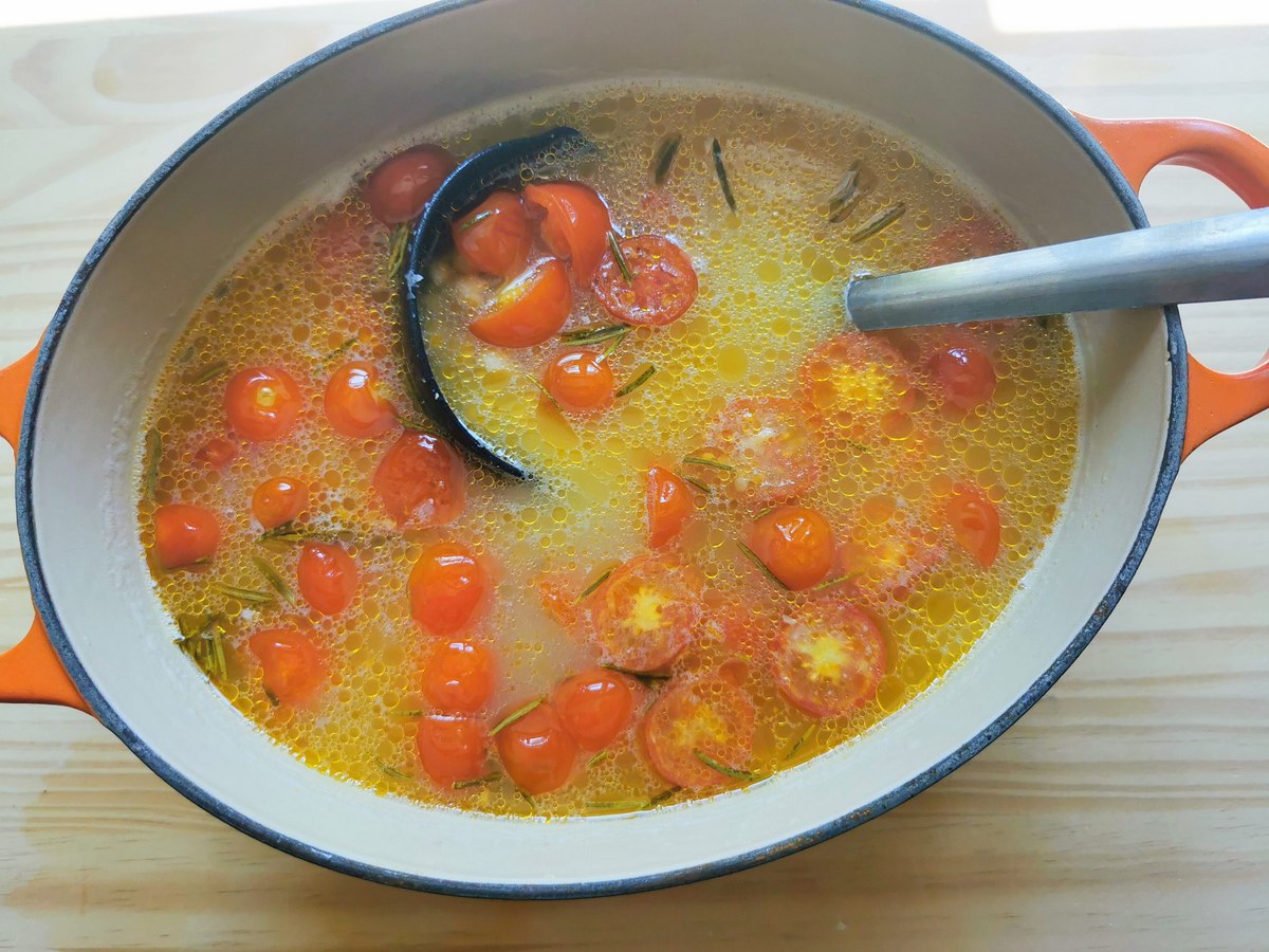 Cooked tomatoes and rosemary added to chickpeas in Dutch oven.