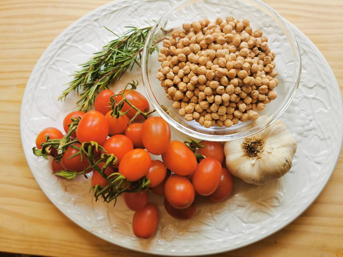 Ingredients for traditional Tuscan chickpea and pasta soup: dried chickpeas, garlic, small tomatoes and fresh rosemary.
