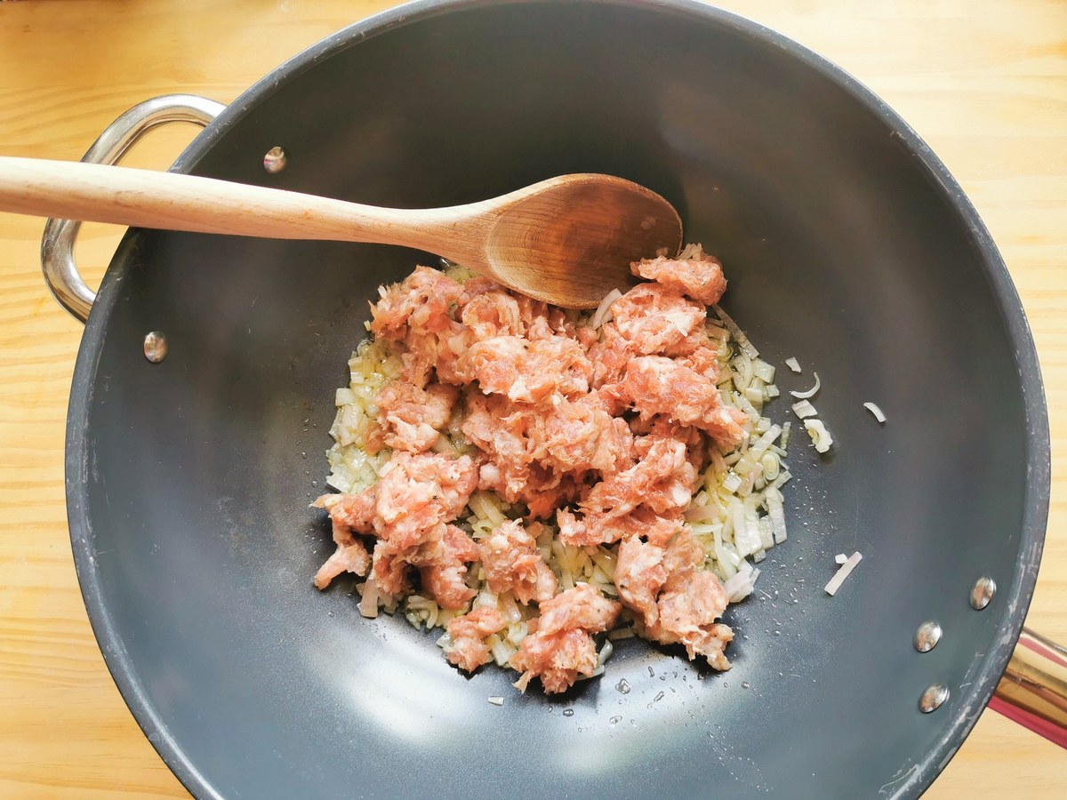 Crumbled pork sausage meat in skillet with cooked onion.