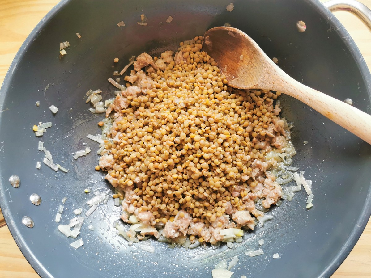 Cooked umbrian lentils added to sausage meat and onion in skillet.