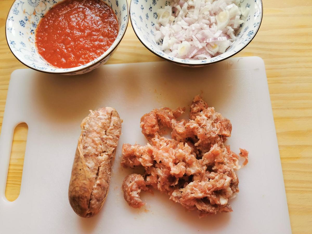 Peeled and chopped onion in small bowl. Crumbled sausage meat on chopping board and tomaato passata in small bowl.