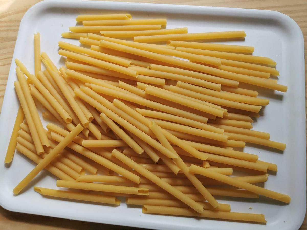 Zitoni pasta broken in half on white tray.