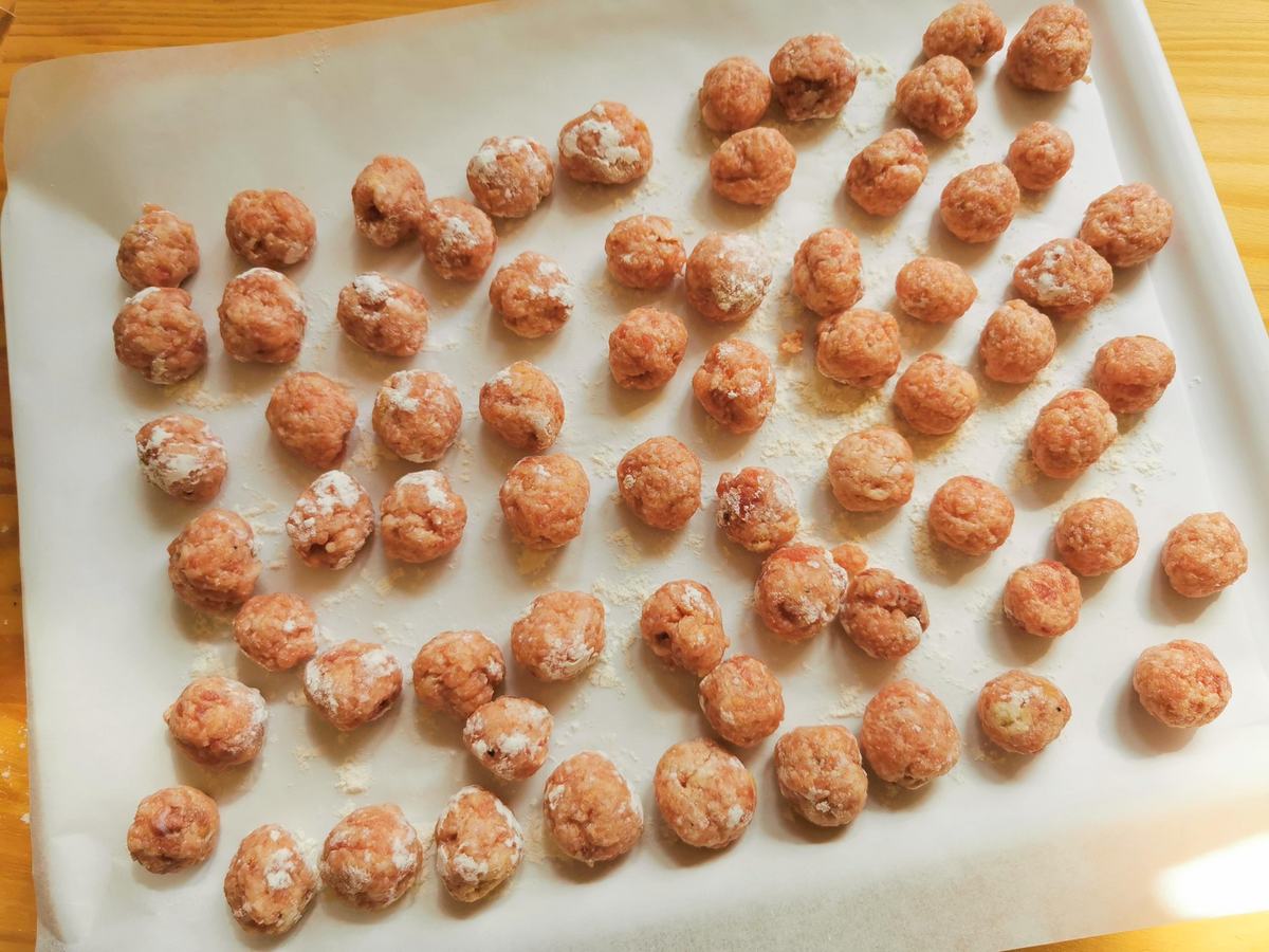 Uncooked meatballs on flour dusted parchment papaer.