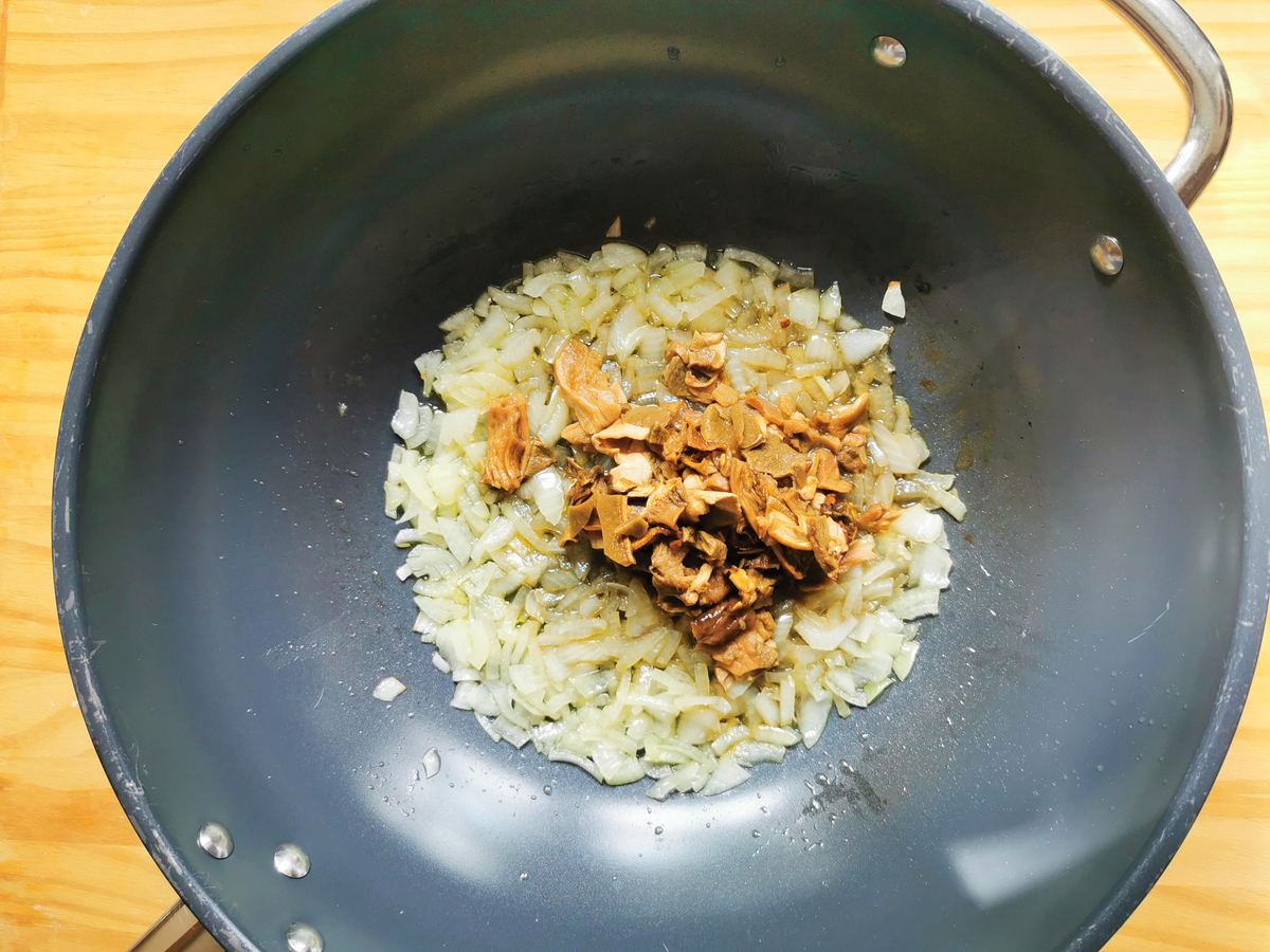 Chopped onion and porcini pieces cooking in skillet.