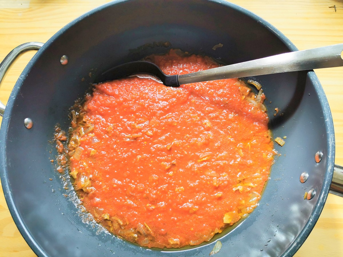 Tomato passata with onion and porcini cooking in skillet.