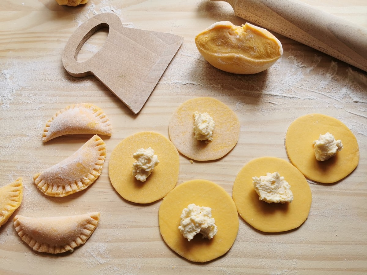 5 circles of ravioli dough with a teaspoon of ricotta filling on them and 3 completed ravioli.