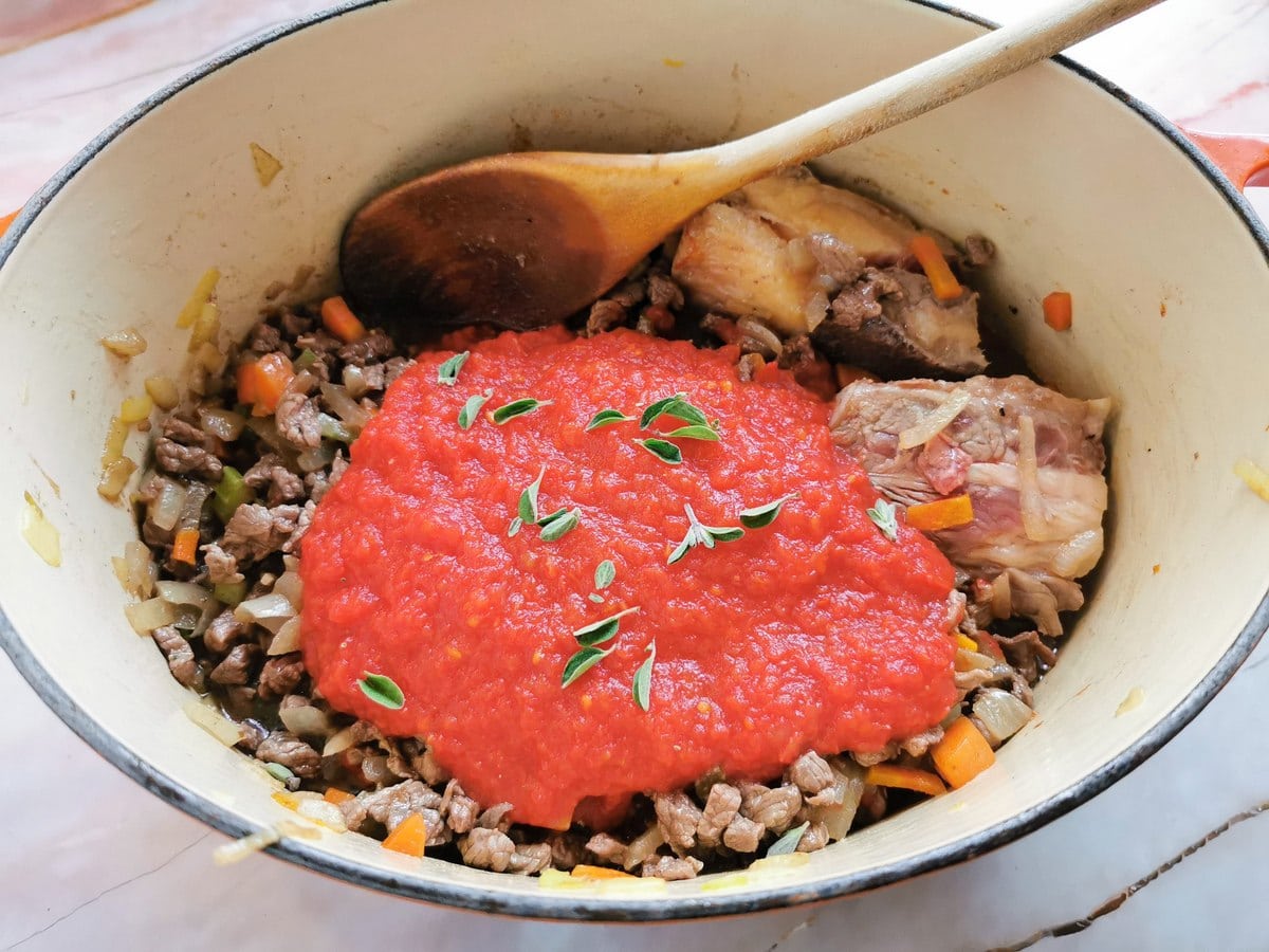 tomato passata and fresh marjoram in Dutch oven with chopped beef, beef bones and vegetables