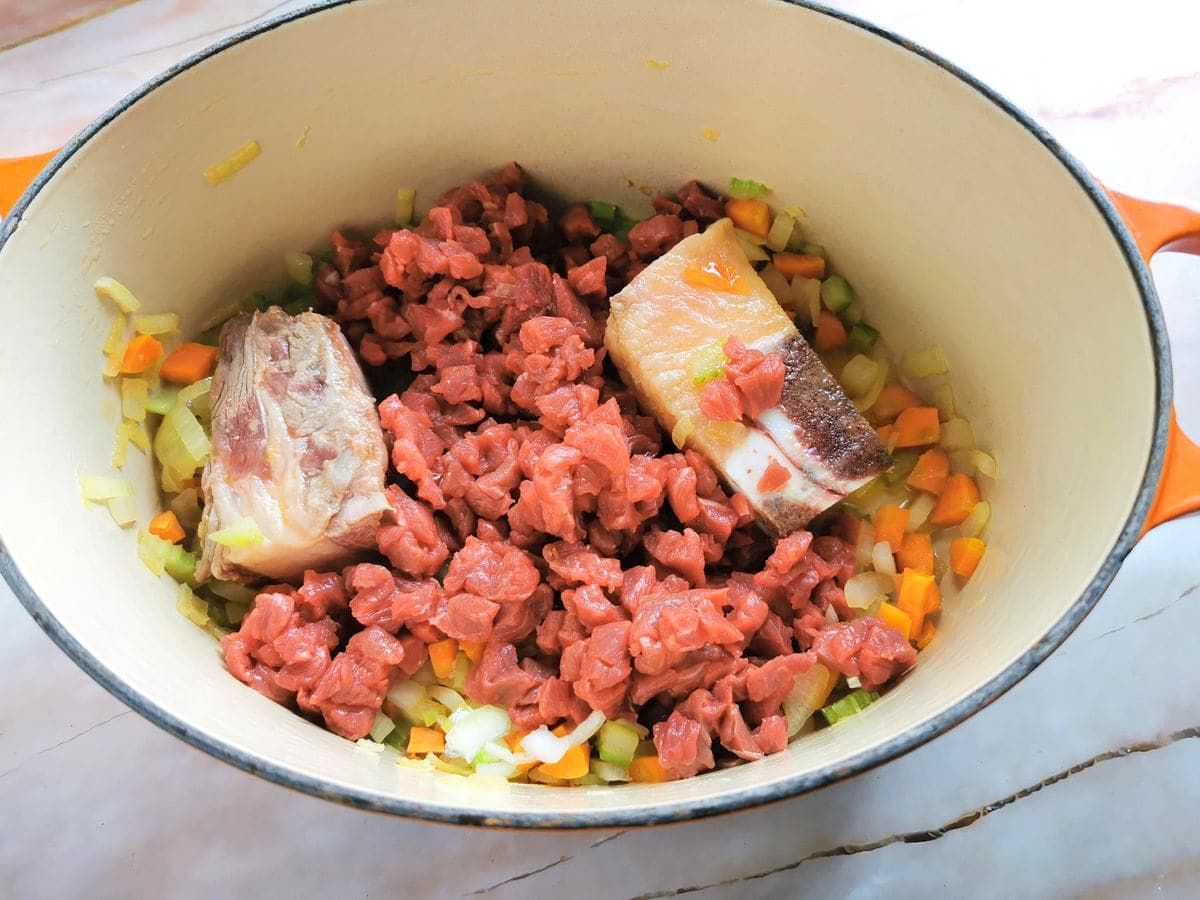 chopped beef in Dutch oven with beef bones and vegetables