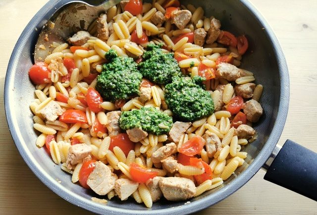 homemade basil pesto added to pasta, tuna and tomatoes in frying pan