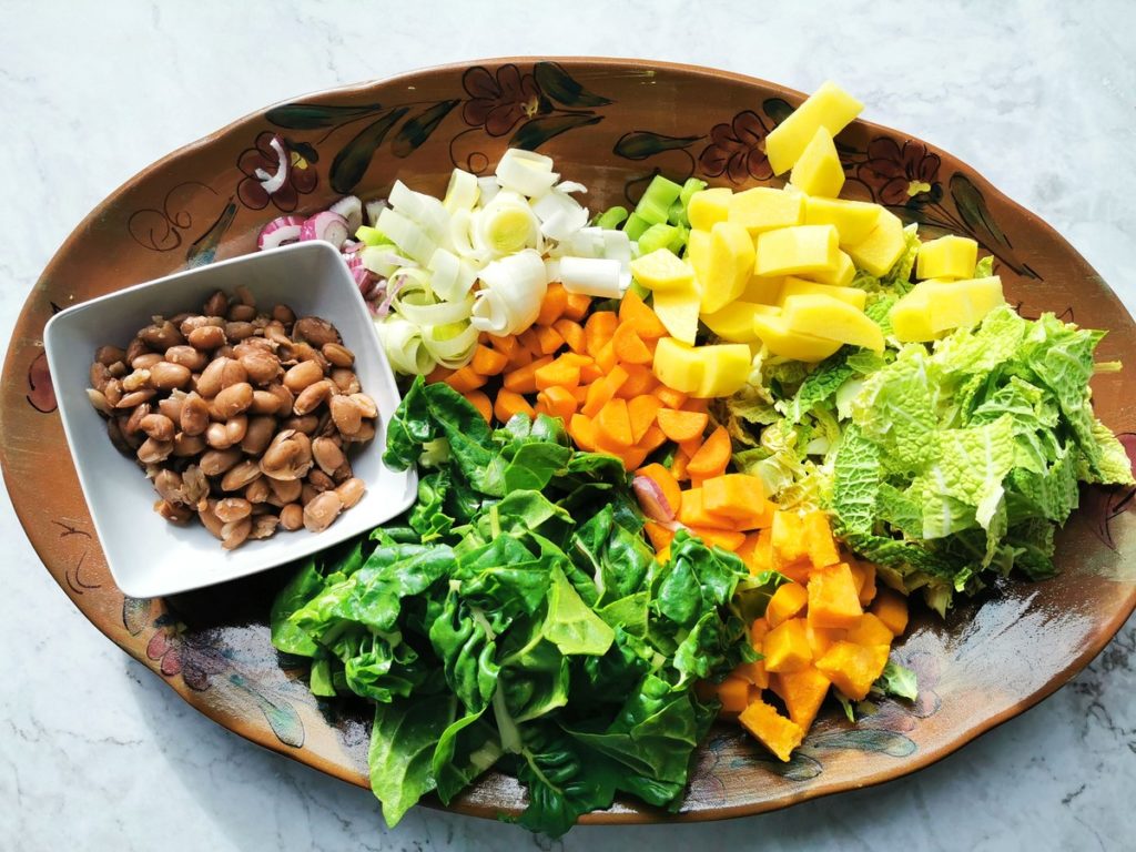 Cooked beans and peeled, washed and chopped vegetables on an oval terracotta plate