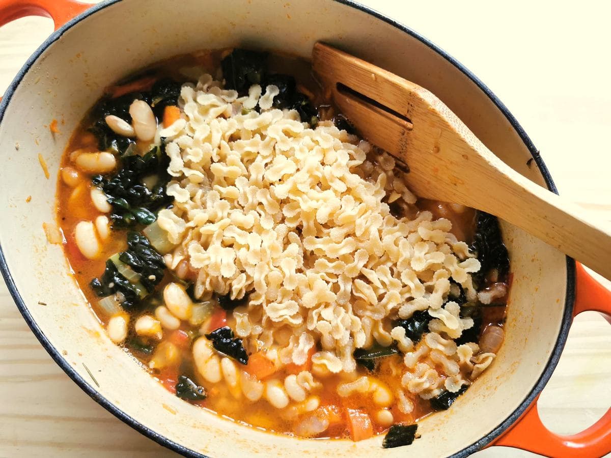 tripolini pasta added to kale and white bean soup in Dutch oven