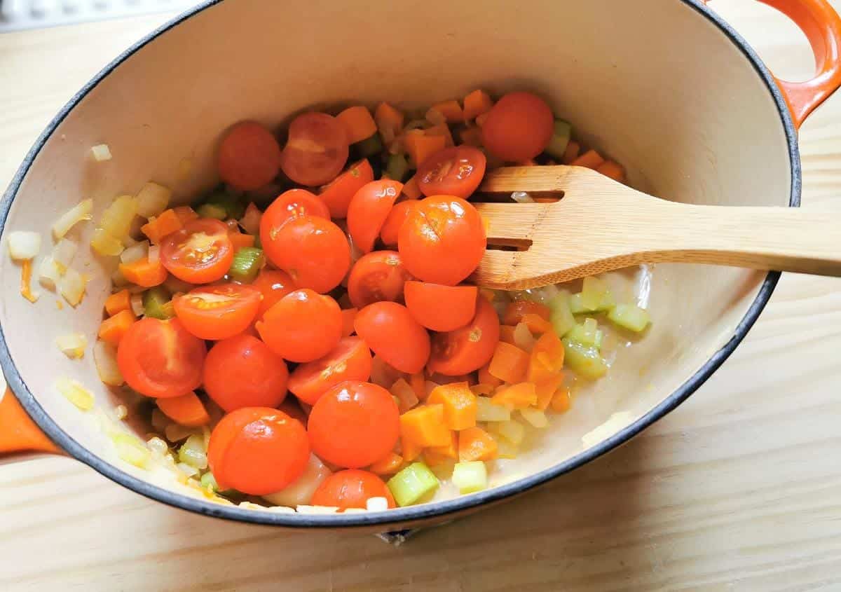 Halved cherry tomatoes in Dutch oven with chopped onions, celery and carrots