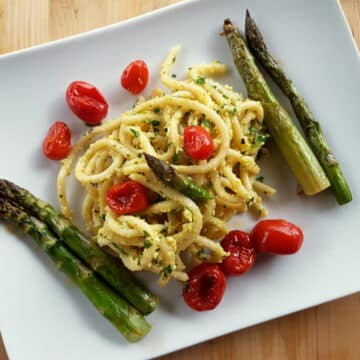 Tuscan pici pasta all'etrusca with asparagus and cherry tomatoes on white plate