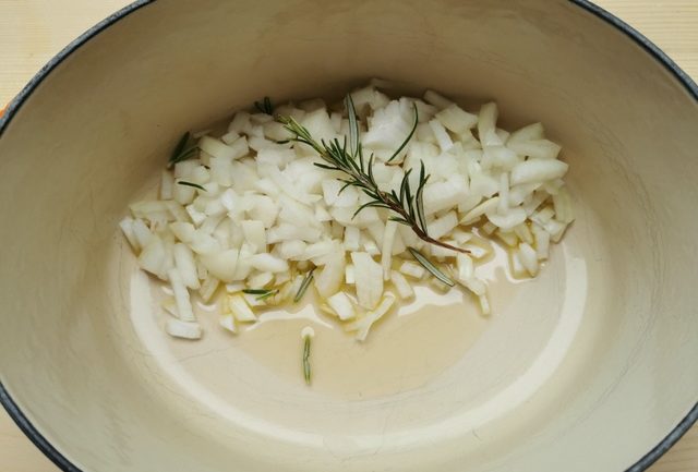 chopped onions, sprig of rosemary and olive oil in Dutch oven