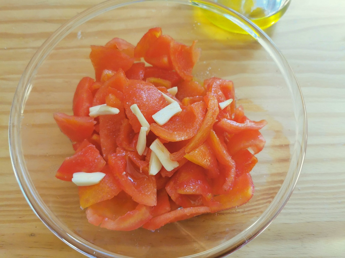 Pieces of peeled and deseeded fresh tomatoes in heatproof glass bowl with slithers of garlic.