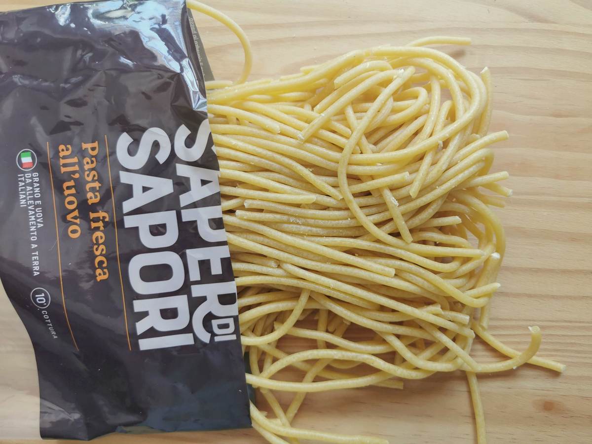 Store-bought fresh bigoli pasta on wood surface.