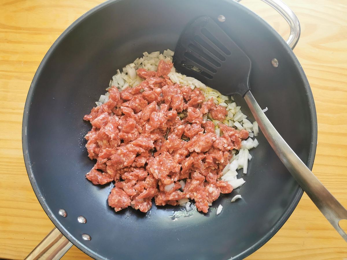 Chopped white onion and crumbled luganega sausage cooking in large skillet.