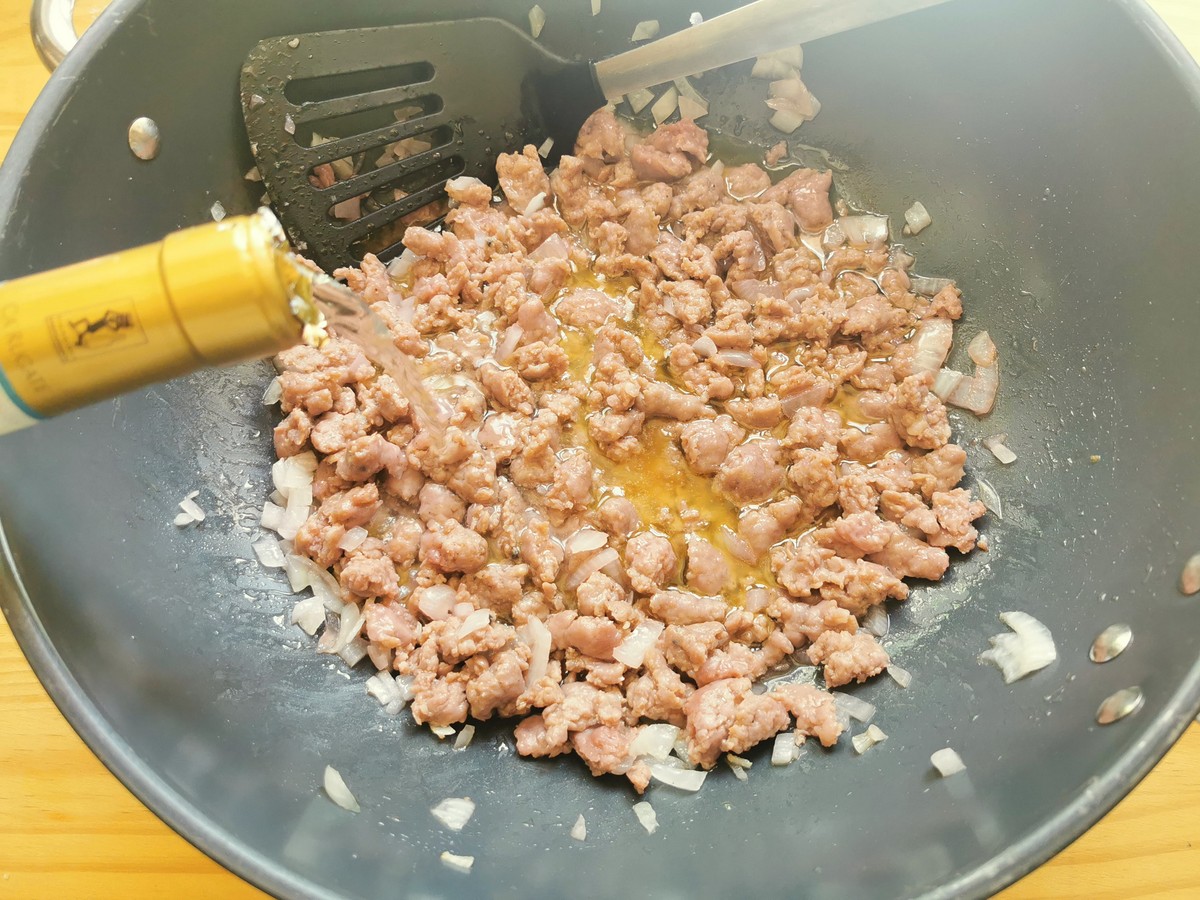 White wine being added to sausage and onion cooking in large skillet.