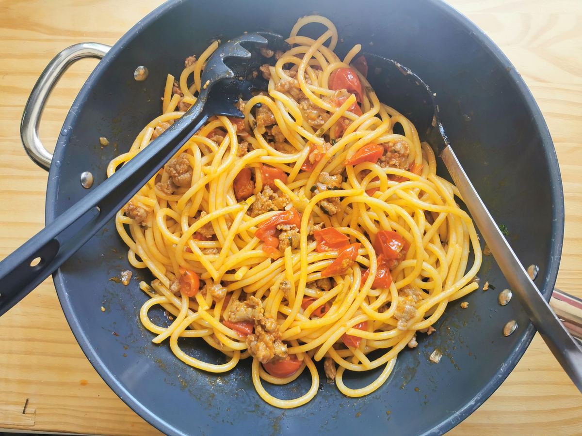 Cooked bigoli pasta mixed with luganega sausage ragu in deep skillet.