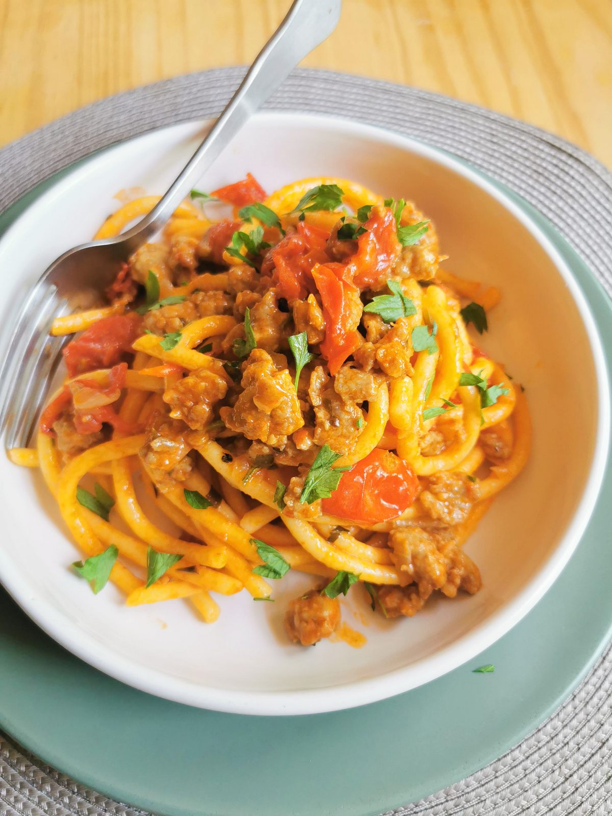 Venetian bigoli pasta with luganega sausage in white bowl with fork.