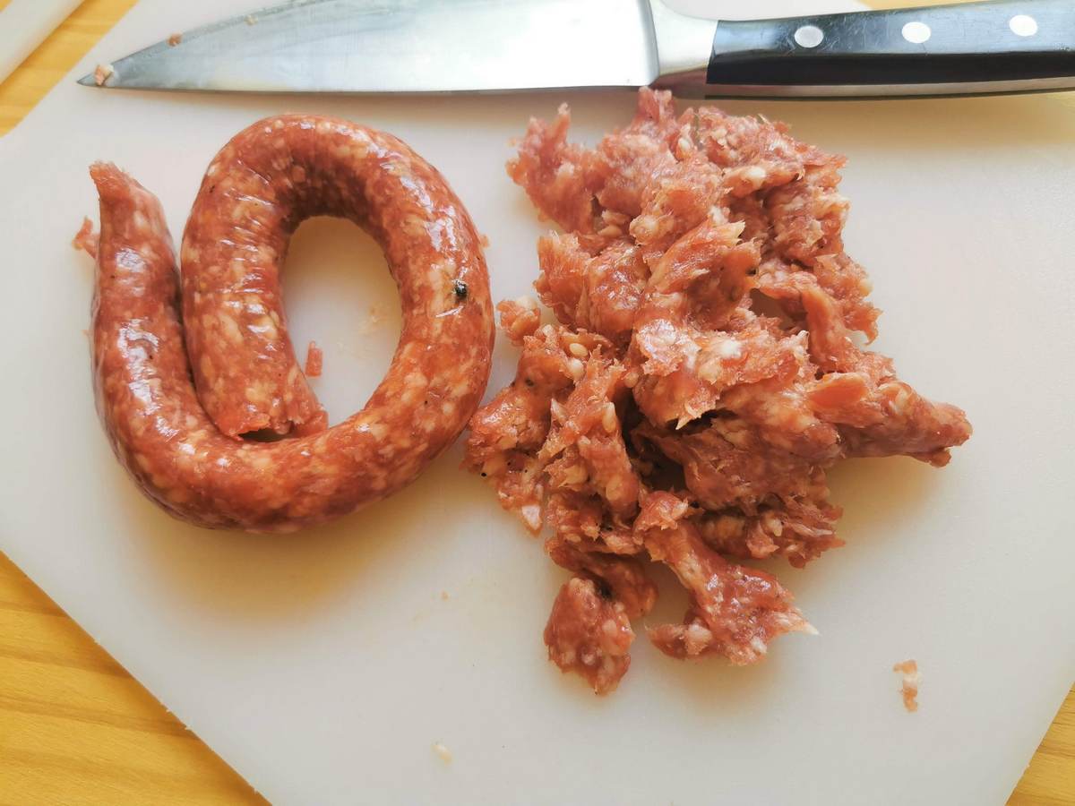 Luganega sausage on white chopping board crumbled into small pieces.