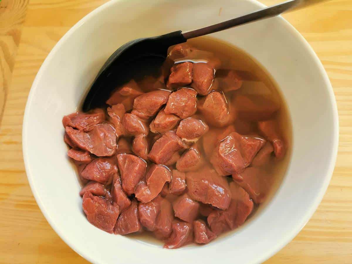 Venison marinating in white wine in a bowl.