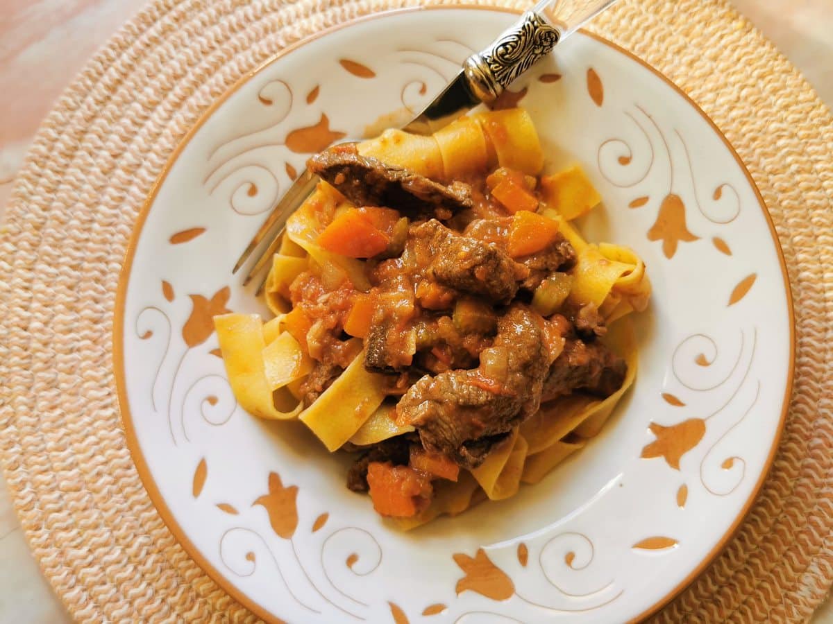 Venison ragu with pappardelle in white and terracotta bowl.