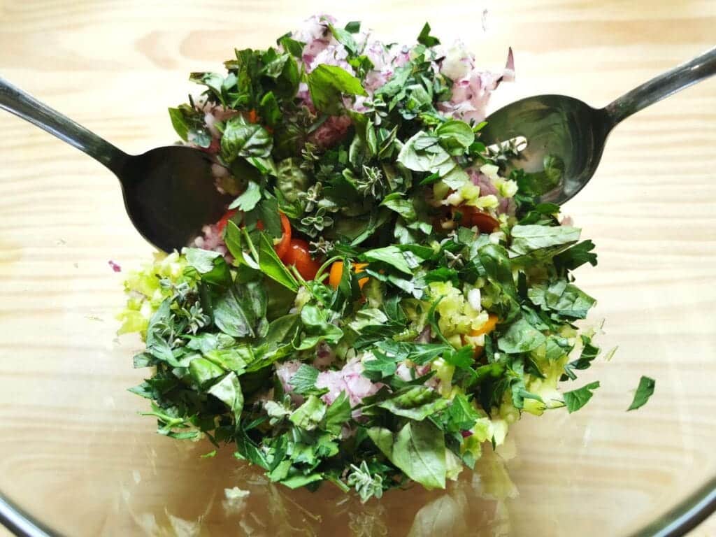 fresh basil, parsley and oregano added to veggies in glass bowl