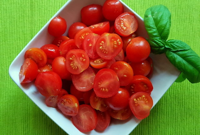 halved cherry tomatoes with basil in a white bowl