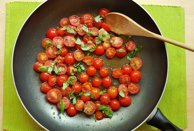 cherry tomato halves with basil and garlic in frying pan