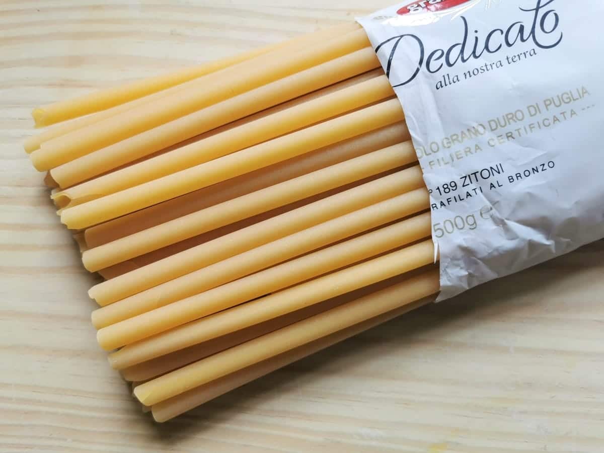Packet of Italian dried zitoni pasta (large ziti) on wooden board