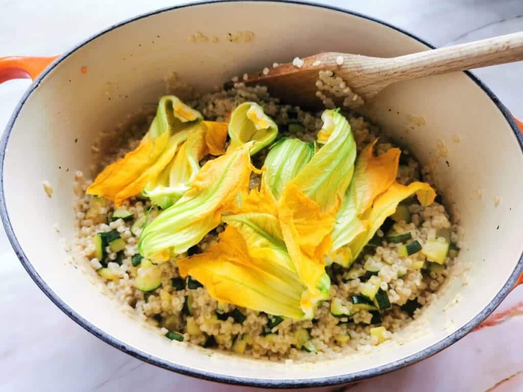 zucchini flowers in Dutch oven with cooked pasta and zucchini.