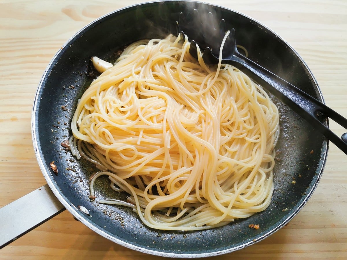 Just cooked spaghetti added to skillet with anchovies, oregano and garlic.