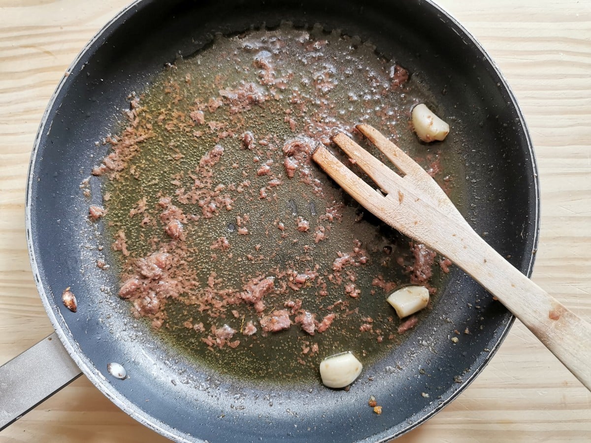 Pieces of anchovies melting in olive oil in skillet.