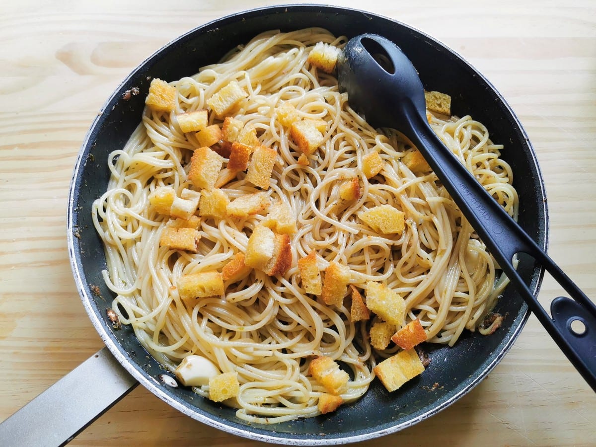 Fried bread croutons in skillet with spaghetti and anchovies.