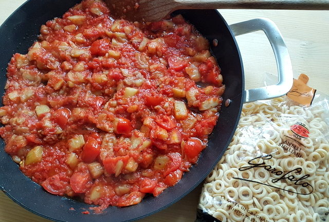 tomato and eggplant sauce in frying pan with packet of pasta nearby