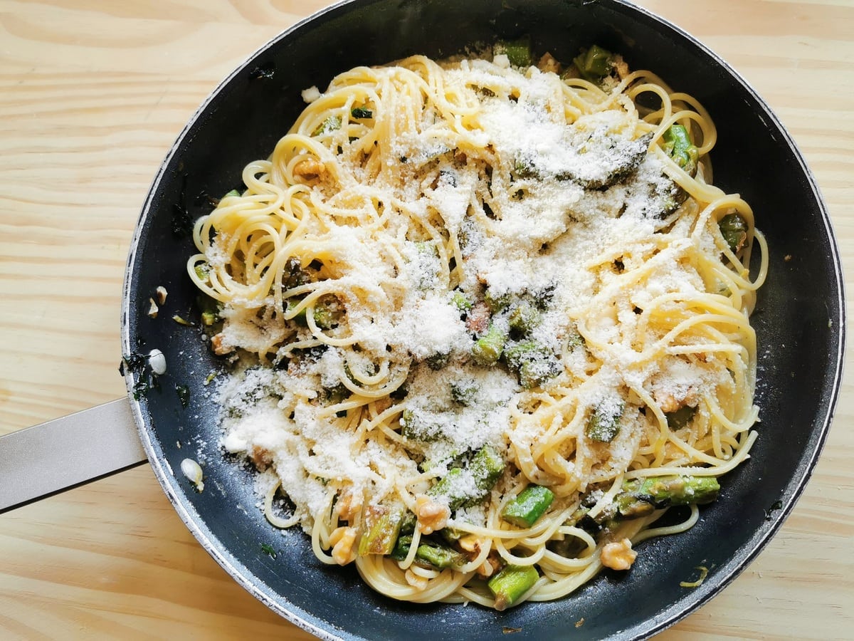 grated pecorino added to asparagus pasta with walnuts in skillet