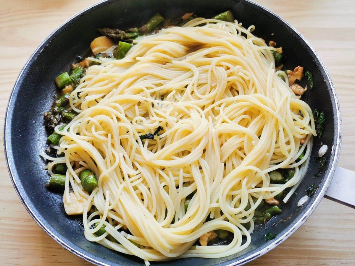 Cooked spaghetti in skillet with asparagus and walnuts
