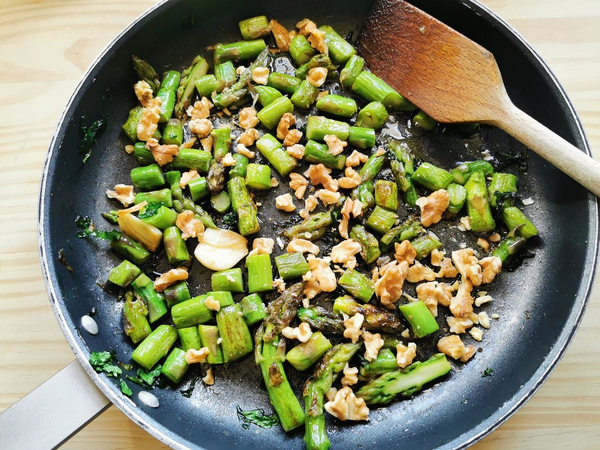 garlic, asparagus pieces and walnut pieces cooking in skillet