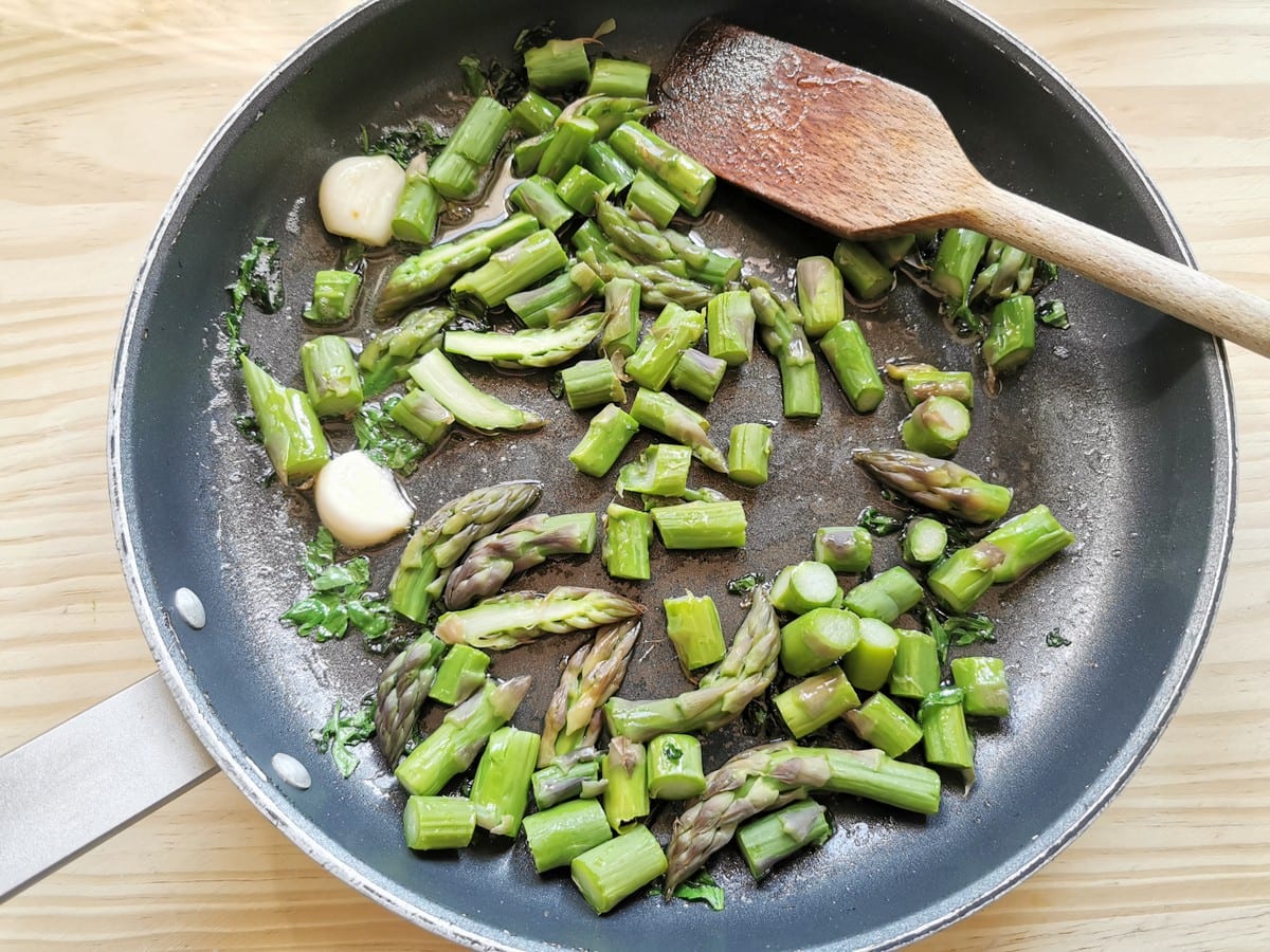 Pieces of asparagus stalks and spears in skillet with parsley and garlic