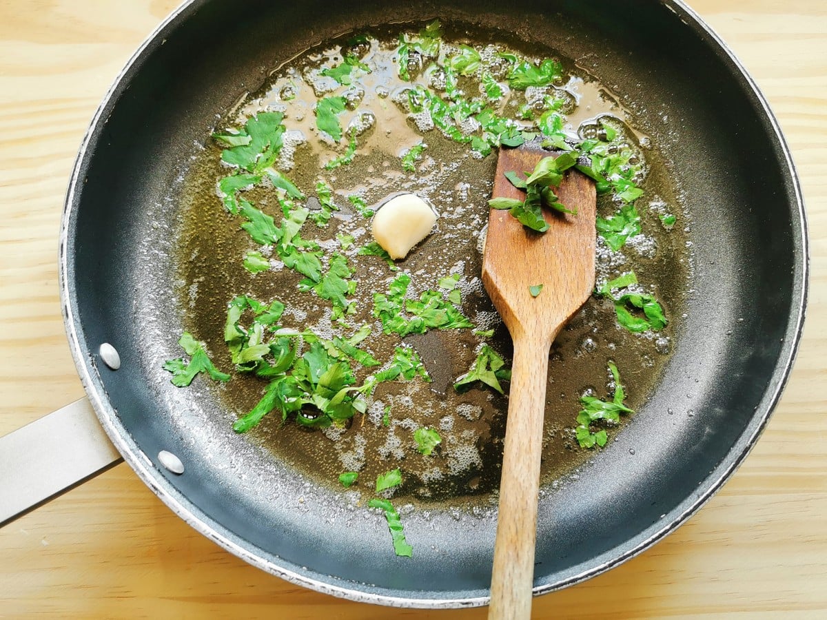 Garlic cloves and chopped parsley cooking in skillet with butter and olive oil