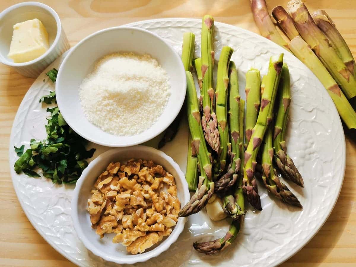 cleaned asparagus, peeled garlic chopped walnuts and parsley and grated pecorino on white plate