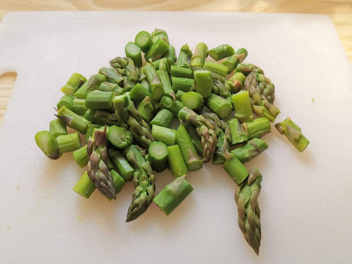 cooked asparagus stalks and spears cut into pieces on white cutting board