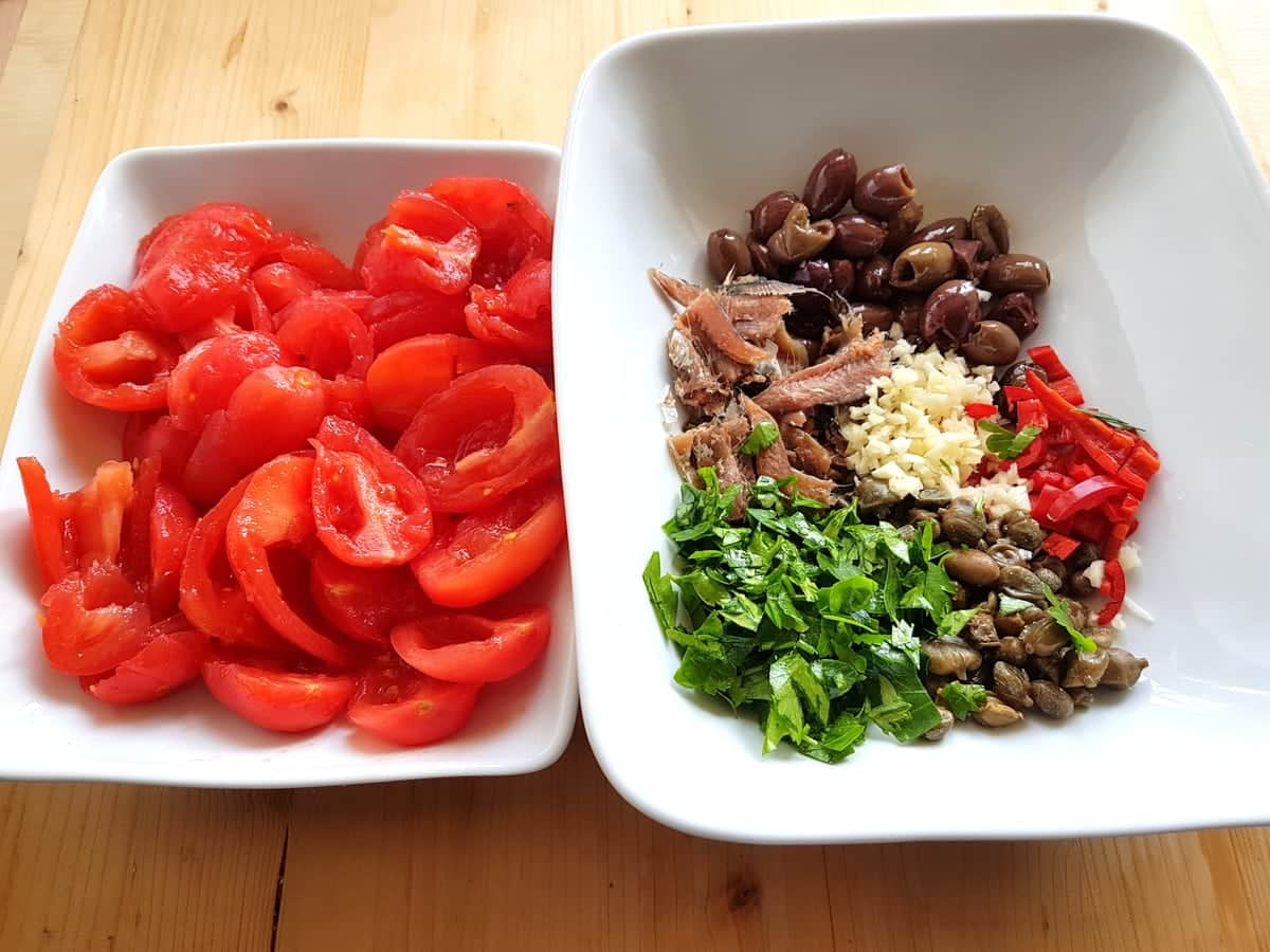 Peeled and chopped tomatoes in white bowl and other prepared ingredients in white bowl.