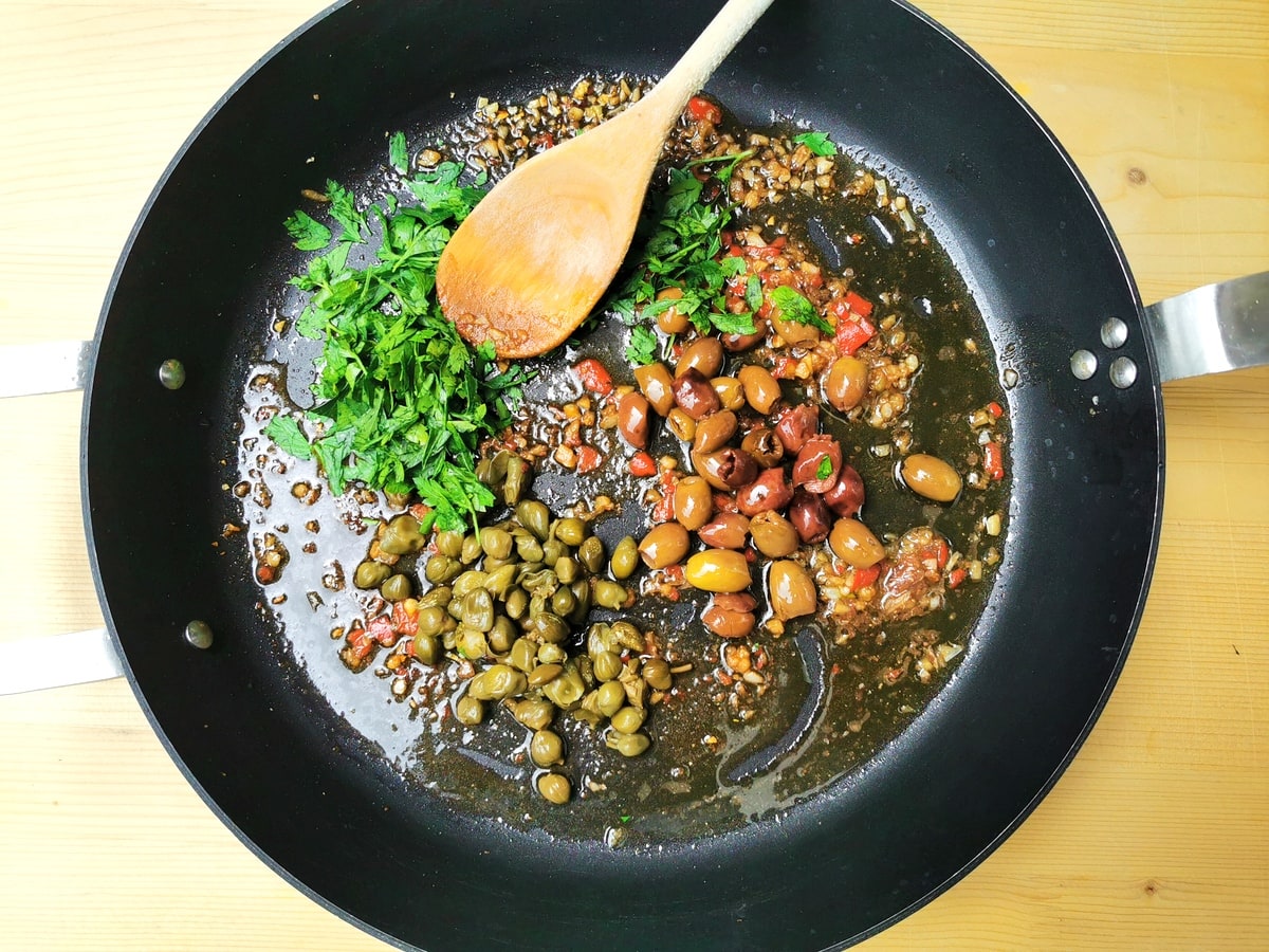 Chopped garlic, anchovies, peperoncino and parsley in frying pan with olives and capers.