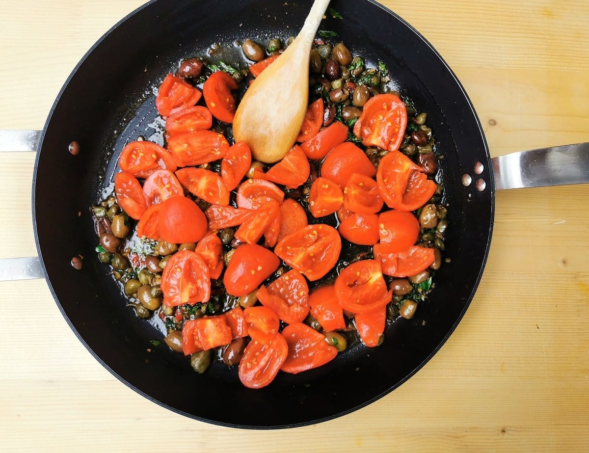 Peeled and chopped tomatoes in frying pan with other puttanesca ingredients.