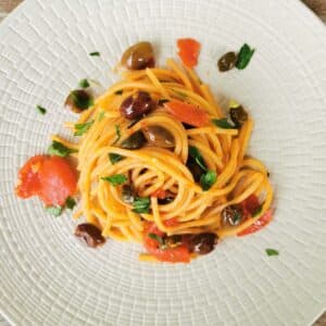 Pasta alla puttanesca garnished with flat leaf parsley.