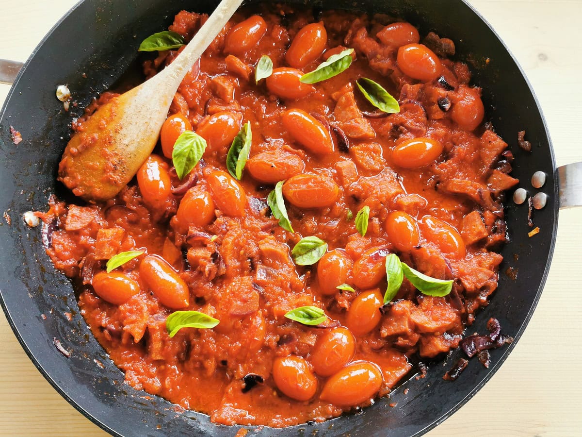 Spicy sausage tomato sauce with basil in a pan.