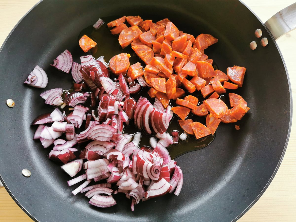 Red onion and sausage cooking in a pan.